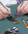 ESD rubber soldering mat on green anti-static workbench; person uses red and black test probes on a circuit board.