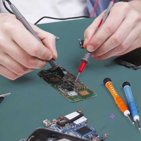 ESD rubber soldering mat on green anti-static workbench; person uses red and black test probes on a circuit board.