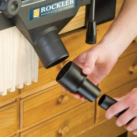 Person holding Dust Port Adapter For One And A Quarter Inch Vacuum Wand To Two And A Quarter Inch Port Vacuum Hose Durable Plastic Dust Collector Accessory For Attaching Shop Vac Dovetail Jig And Other Tools near a woodworking setup.