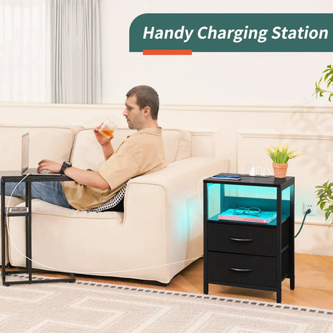 Man using USB nightstand with charging station, LED light fabric drawers, black bedside table, small modern design.