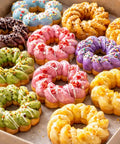 Colorful variety of donuts topped with icing and sprinkles, showcasing the result of using a Straight Up Heavy Duty French Cruller Plunger Extruder.