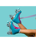 Legs wearing turquoise roller skates with pink laces against blue background, wheels showing 78A Outdoor Indoor Quad Roller Skate Wheels 65x35mm ABEC9 Bearings Eight Pack Sea Blue Durable Gummy PU For Smooth Ride On Street Park Or Rink Excellent Vibration Dampening And Grippy Traction.