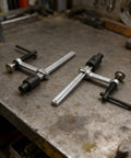 Two Pack Quick Action Bench Dog Clamps For 16mm Holes Hold Down Clips on workbench, silver black metal, ergonomic grip.