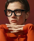 Person wearing black Wayfarer-style glasses looking thoughtful