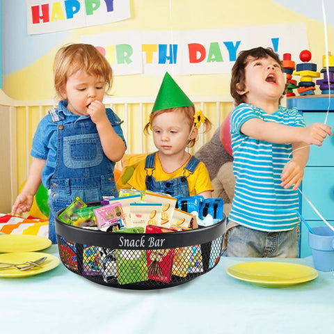 Black metal four-compartment snack organizer on countertop, spinning Lazy Susan with divider, filled with snack packets.