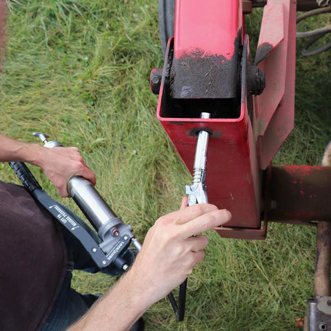 Side view of LockNLube XL grease gun coupler on a grease gun reaching a red recessed fitting outdoors.