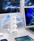 Power Strip Tower With 12 AC Outlets And 4 USB Ports 2 USB C 2 USB A For Home Office Dorm Room Flat Plug Surge Protector 6ft Cord Charging Station 16 In 1 White on a desk near a laptop, charging multiple devices.