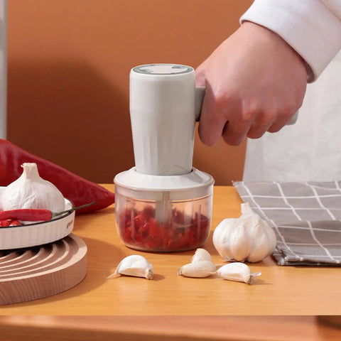 Cordless Electric Hand Mixer With Stainless Steel Beaters. USB Rechargeable Power For Quick Whipping And Blending Eggs Or Cream. Three Speed Settings Ensure Smooth Mixing Every Time. Ergonomic Grip Makes Baking Easy And Fun For All Skill Levels At Home. Hand using a cordless mixer on garlic and peppers.