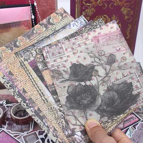 Hand holding floral scrapbook paper from All In One Vintage Junk Journal Kit With 185 Pieces Scrapbook Paper Pack A6 Aesthetic Notebook Scrapbook Kit Art Craft Diy Gift For Adults Women Starter Friendly in front of embellishments and patterned book cover in background.