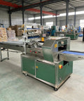 Compact Horizontal Flow Wrapper Shrink Wrap Machine 50 To 80 Pieces Per Minute in a warehouse setting with packaging materials nearby.