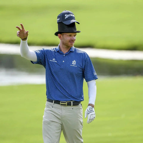 Golfer in blue shirt gestures on course, wearing Men's Golf Ratchet Belt With Adjustable Leather Strap, casual style.