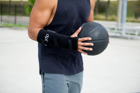 Person wearing a Red Light Therapy Wrist Wrap For Pain Relief And Carpal Tunnel Support while holding a basketball outdoors.