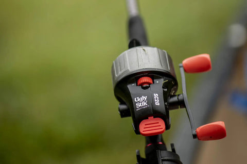 Close-up of a black and red spincast reel mounted on a fishing rod, labeled "Ugly Stik" and "SC20".