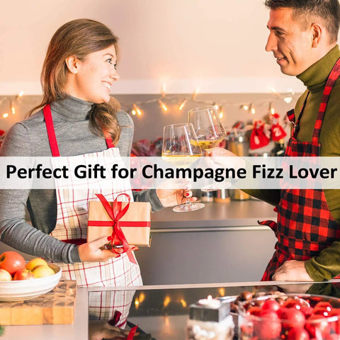 Two people toasting with champagne in a decorated kitchen, wearing aprons, holding a gift, promoting 2 Pack Champagne Stoppers With Built In Vacuum Pump Black Keeps Bubbles Fresh To The Last Drop And Keeps It Fizzy With A Game Changing Pump Piston System For A Tight Seal And Leak Proof Sparkling Wine Saver.