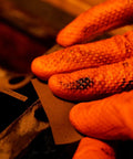 Orange nitrile gloves, close-up of diamond-textured fingers gripping a metal sheet