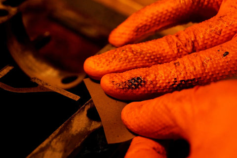 Orange nitrile gloves, close-up of diamond-textured fingers gripping a metal sheet