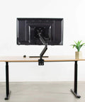 Built Tough VESA Adapter Bracket For TVs And Monitors Max 42 Inches mounted on desk with black monitor arm and plant.