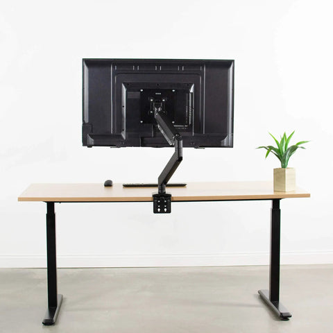 Built Tough VESA Adapter Bracket For TVs And Monitors Max 42 Inches mounted on desk with black monitor arm and plant.