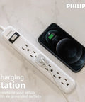 Six Outlet Surge Protector Power Strip With A 2 Ft Cord, 450 Joules Surge Protection, next to a charging smartphone on a desk.