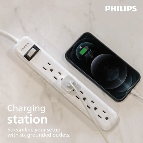 Six Outlet Surge Protector Power Strip With A 2 Ft Cord, 450 Joules Surge Protection, next to a charging smartphone on a desk.