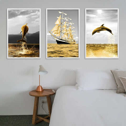 Room interior with three framed artworks featuring dolphins and a sailing ship above a bedside table and lamp.