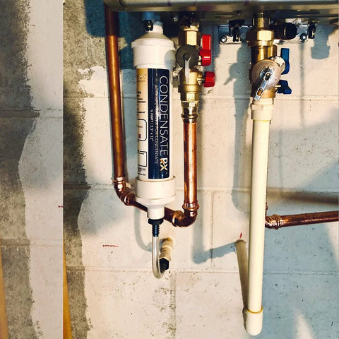 CondensateRx condensate neutralizer, white cylindrical unit installed on copper piping under boiler