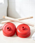 Rock Solid Heavy Duty Rubber Cup Toilet Plunger With Reinforced Wooden Handle and two red rubber cups on a clean surface.