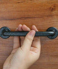 Hand holding Rustic Antique Black Cabinet Pulls Curved Zinc Alloy 5.5 Inch Length with 5 Inch Hole Center mounted on wood.