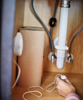 Person installing Flo Smart Water Leak Detector 3 Pack under sink, monitoring for costly damage in kitchen plumbing.