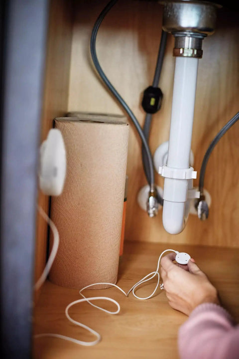 Person installing Flo Smart Water Leak Detector 3 Pack under sink, monitoring for costly damage in kitchen plumbing.