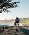 Cyclist on coastal road with Lumina 1000 Boost Front Bike Light With Sabre 110 Rear Light, mountain backdrop