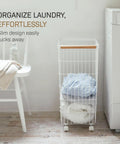 Rolling Wire Laundry Hamper With Wood Accent next to white chair and washing machine, showing its slim design in small space.