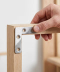 Hand holding 100-Piece Stainless Steel L-Shape Corner Bracket Set for 2x2 Inch Small Angle Joints on wooden frame