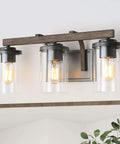 Rustic Faux Wood Three Light Farmhouse Vanity Light With Clear Glass Shades Distressed Black Backing And Decorative Panels