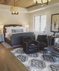 Cozy bedroom featuring a gray bed, leather chairs, and a patterned rug, showcasing a warm interior design.
