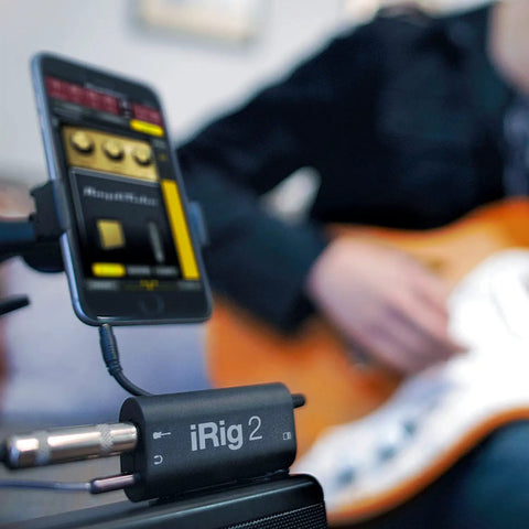 iRig 2 Portable Guitar Interface for iPhone iPad and Mac with cable connected, musician playing guitar in background