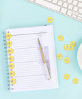 Gold Brass Washers And Paper Brads 500 Piece Set For Paper Crafts Scrapbooking And DIY Projects 15mm Outer Diameter 3mm Inner Diameter Metal Fasteners With Storage Box Included scattered on notebook with pen.