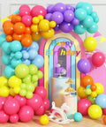 Rainbow Balloon Arch Kit With 80 Latex Balloons In 12 And 10 Inch Sizes Dope Neon Purple Teal Hot Pink Light Blue Light Green Matte Yellow And Lemon Hues Perfect Pool Party Vibes For Tropical Theme Carnival Decor For Kids Birthday displayed in a colorful arch around a pink and blue birthday setup.