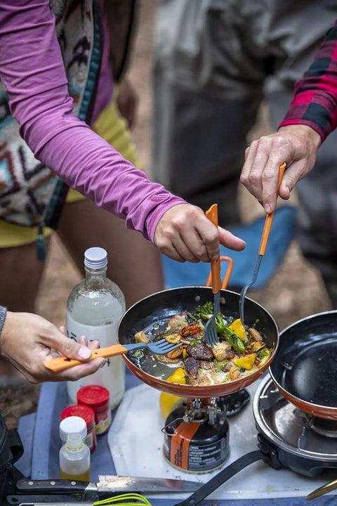 Cooking vegetables on ultralight camping stove that boils water in about 3 minutes during a camping trip, people using utensils.