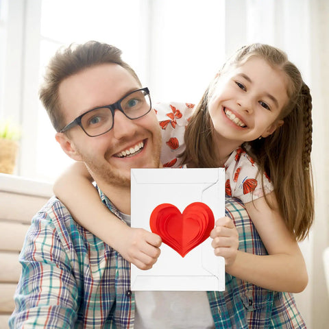 Smiling father and daughter holding a card with a red heart, showcasing 100 Pcs 6.5 By 4.5 Inch Rigid Mailers With Self Seal Envelopes Stay Flat Cardboard Mailers For Shipping Postcards Calendars Photos CDs Documents Comic Books And More