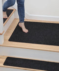 Woman stepping on anti skid black No Slip Carpet Stair Treads 8 By 30 Inches Pack Of 28 With Reusable Adhesive on wooden stairs.