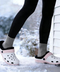 Person wearing white clogs with black fuzzy liners in snow, showcasing Two Pairs Black Fuzzy Clog Liners Warm Removable Insoles For Indoor Outdoor Wear Size 37 38 Replacement Fur Insert For Cozy Winter Steps With All Day Comfort And Cushioned Support.