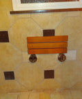 20 Inch Teak Shower Seat Fold Down Wall Mounted Chair against tiled wall, showing durable chrome hinges for space saving use.