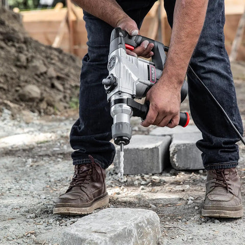 Person using Electric SDS-Plus Rotary Demolition Hammer 1180W With 1-1/4 Inch Bit Capacity to drill into concrete blocks.