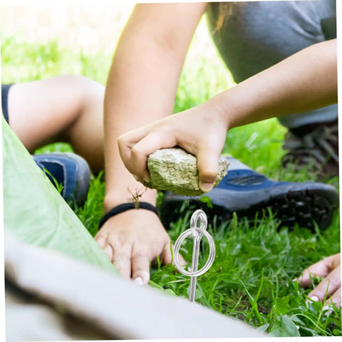Person securing tent with a stake using a rock, highlighting the use of 10 Pack Galvanized Tent Pole Connectors For Quick Setup And Lightweight Repair Camping Must Haves For Hiking And Outdoor Adventures Durable Easy To Use Keeps Shelters Secure.