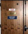 Wooden door with three 'Janitor's Closet' signs in different colors and materials, illustrating Standard Black Janitor's Closet Sign With Adhesive Tape For Easy Stick On Mounting, Durable Wall Signage With Clear Engraved Message, No Drilling Needed, Medium 1 Pack.