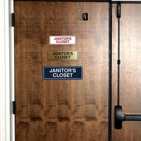 Wooden door with three 'Janitor's Closet' signs in different colors and materials, illustrating Standard Black Janitor's Closet Sign With Adhesive Tape For Easy Stick On Mounting, Durable Wall Signage With Clear Engraved Message, No Drilling Needed, Medium 1 Pack.