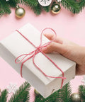 Hand holding gift wrapped in 24x36 inch moving newsprint packing paper with red twine, surrounded by holiday decorations.