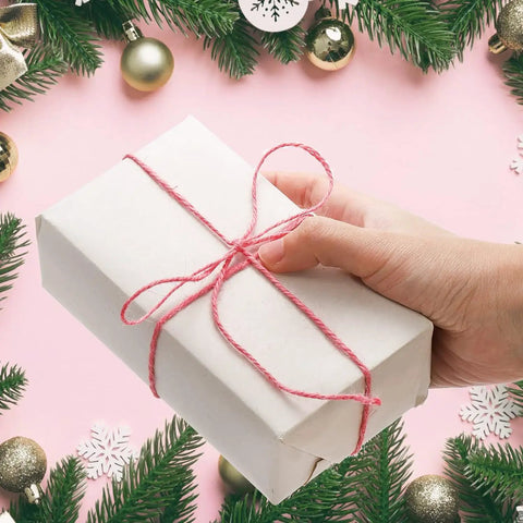 Hand holding gift wrapped in 24x36 inch moving newsprint packing paper with red twine, surrounded by holiday decorations.
