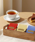 Three Compartment Wooden Tea Bag Box With Handle Acacia Wood Caddy holding colorful tea packets on a table